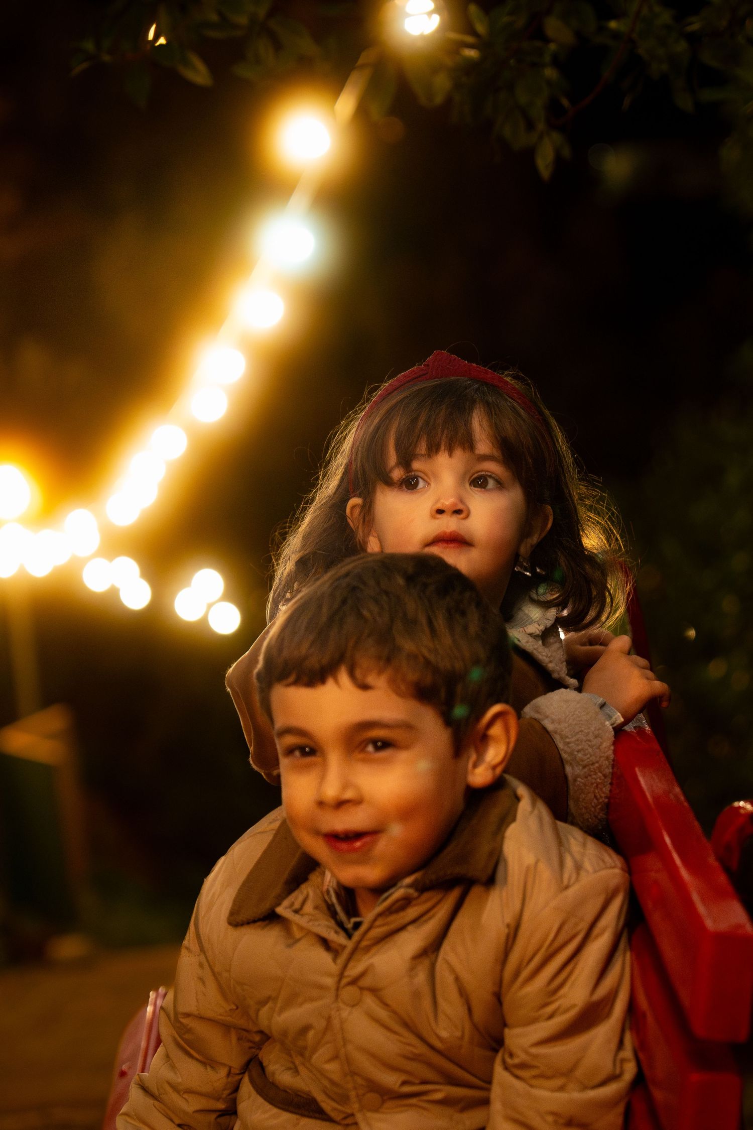 Children illuminated by warm glowing lights in an evening outdoor setting.