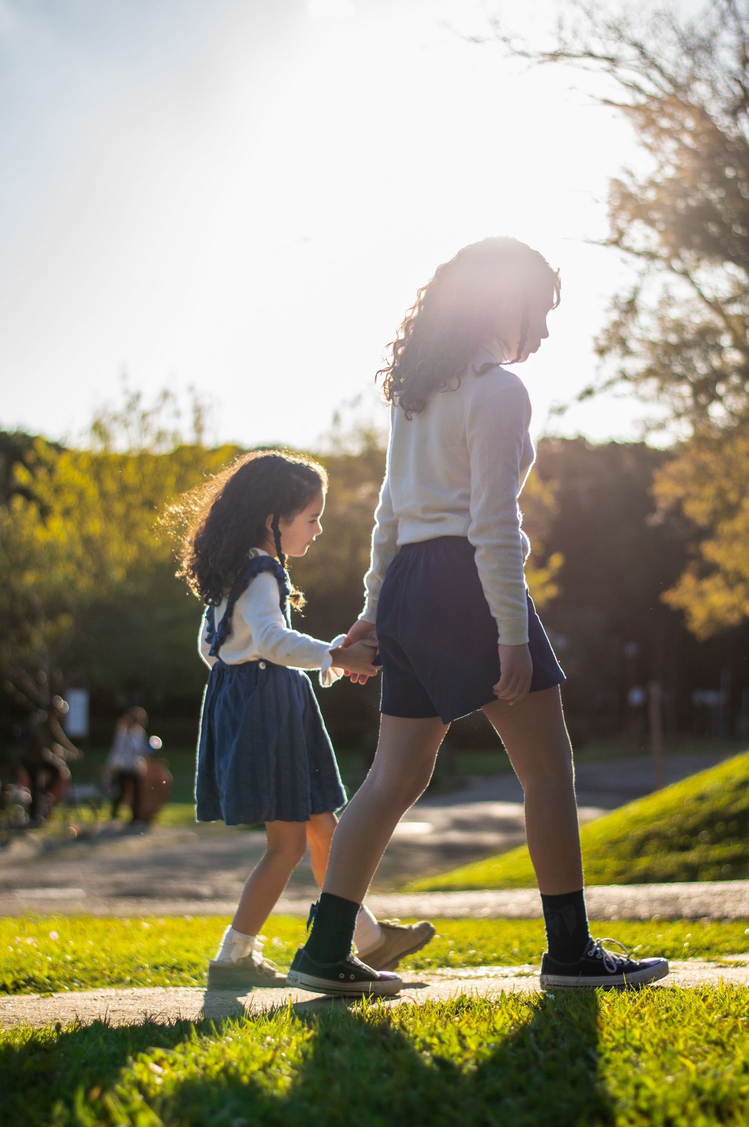 Two figures walking together on a sunlit grassy path during golden hour.