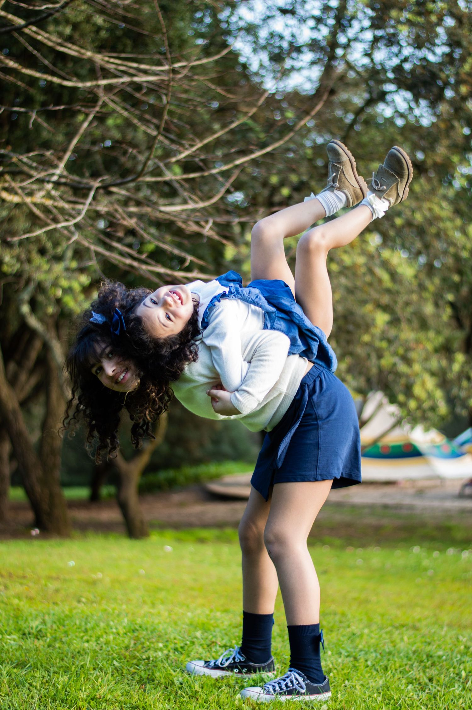 Student in school uniform playfully bending backwards on a grassy lawn.