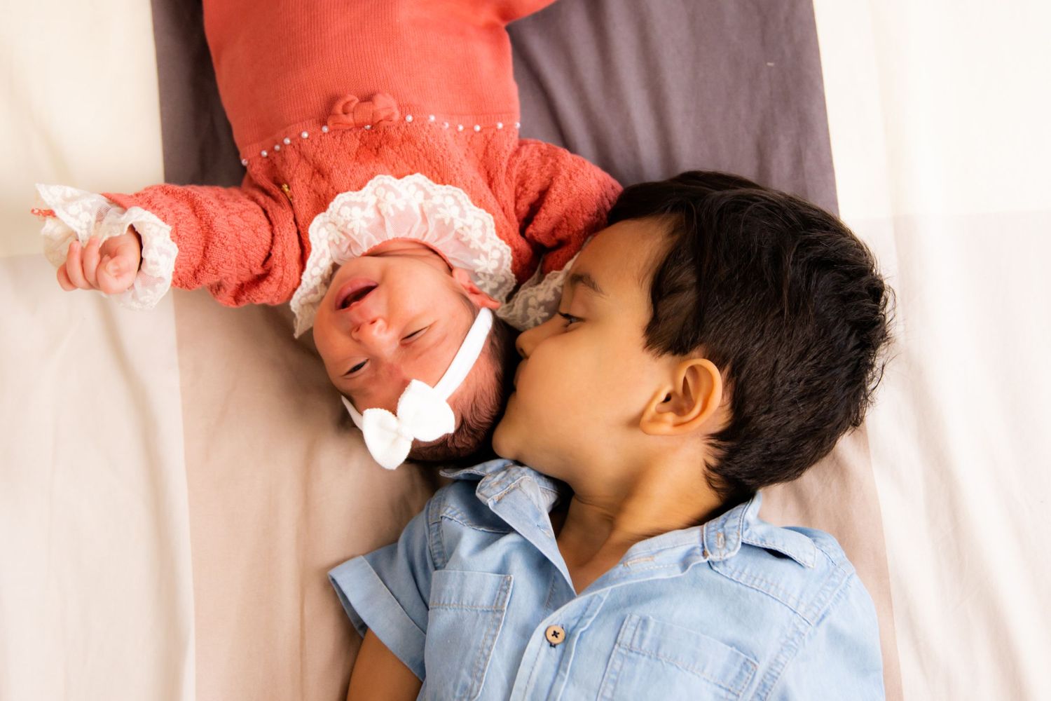 Sweet candid moment of siblings laying together on white bedding.