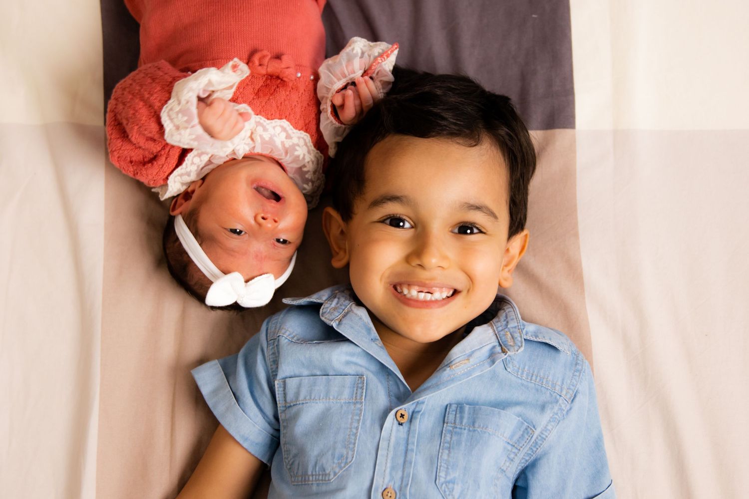 Joyful portrait of siblings laying together on plaid bedding.
