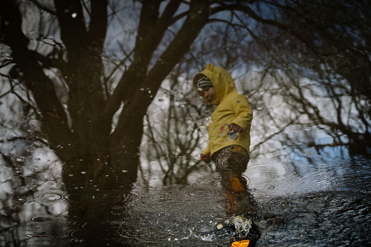 Person in yellow raincoat jumping and splashing in rain puddle.