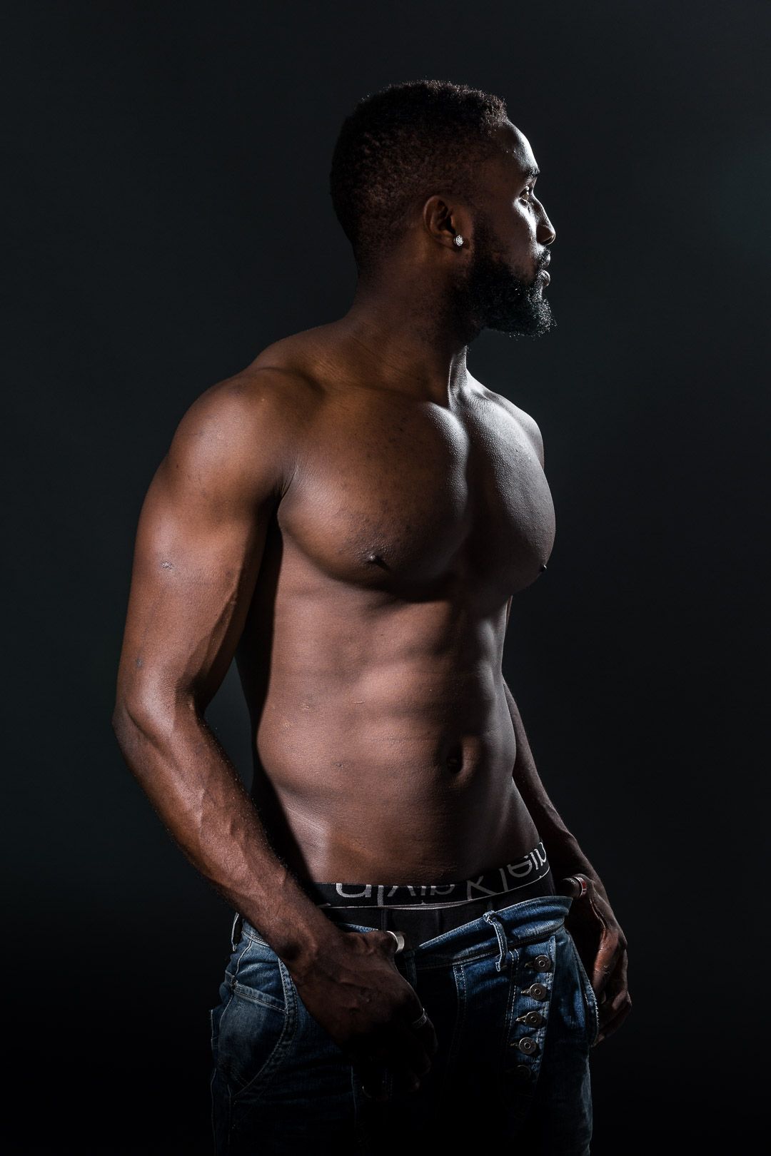 Athletic shirtless figure poses against dark background showing muscular physique.