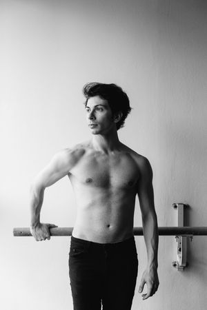 Athletic figure poses at ballet barre in minimalist black and white studio setting.