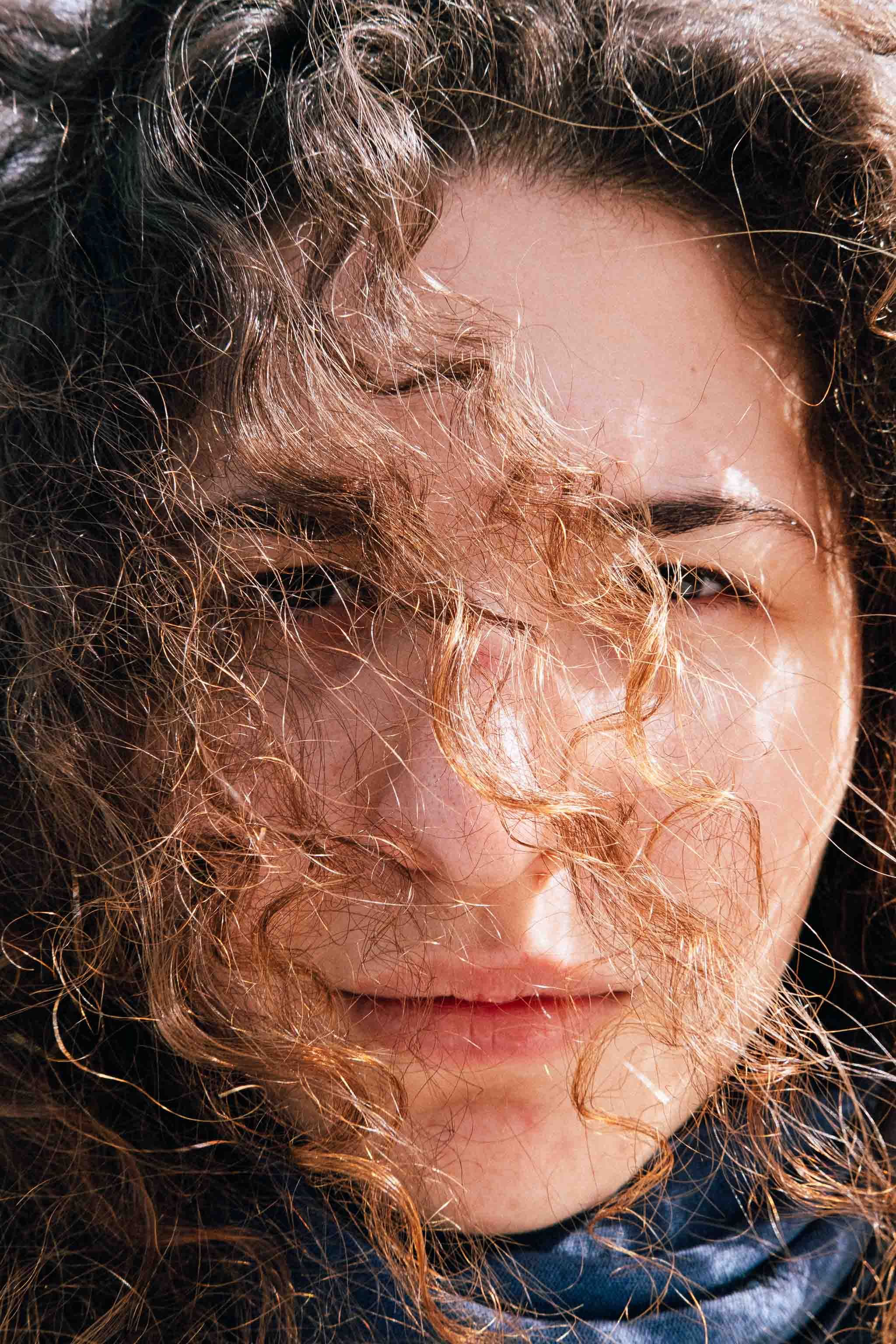 Close-up portrait of a person with windswept curly hair in natural sunlight.