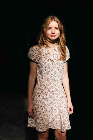 Young person wearing a floral vintage-style dress stands against a dark background.