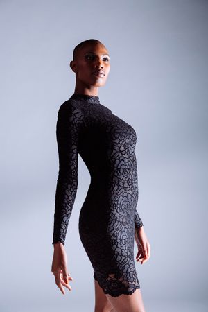 Elegant black lace dress with long sleeves shown in artistic studio portrait against light background.