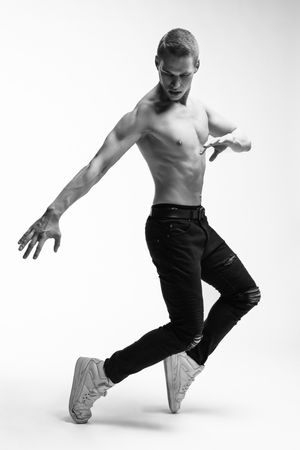Dynamic dance pose of performer in ripped jeans and sneakers against white background.