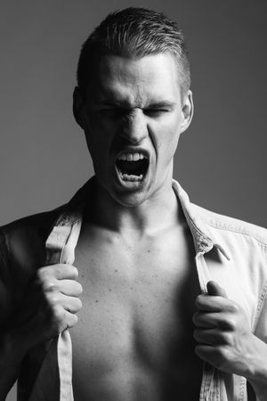 Dramatic black and white portrait of model in unbuttoned white shirt showing intense expression.