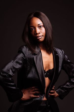 Portrait of model in black blazer and lace bralette against dark background.