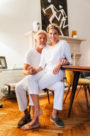 Mature couple in all-white outfits sitting casually together in modern living room.