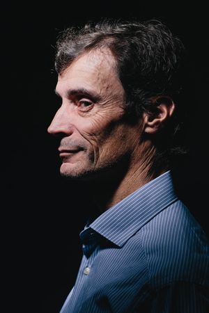 Profile portrait of man in blue striped shirt against dark background.