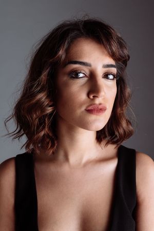Dramatic portrait of woman in black tank top with wavy brown hair against grey background.