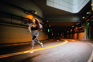 Athletic person jogging through an illuminated underground tunnel at night.