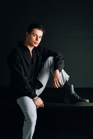 Dramatic studio photo of a person in black shirt and light pants against dark background.