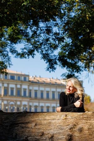 Outdoor portrait against historic building with person leaning on fallen tree trunk.