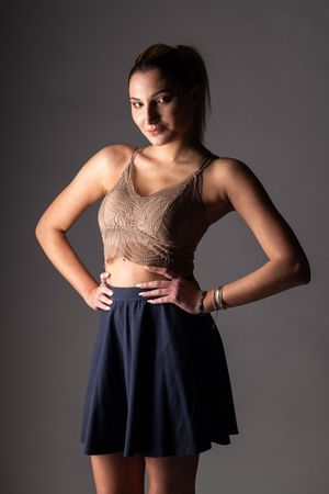 Fashion portrait of a person in crop top and navy skirt against gray background.