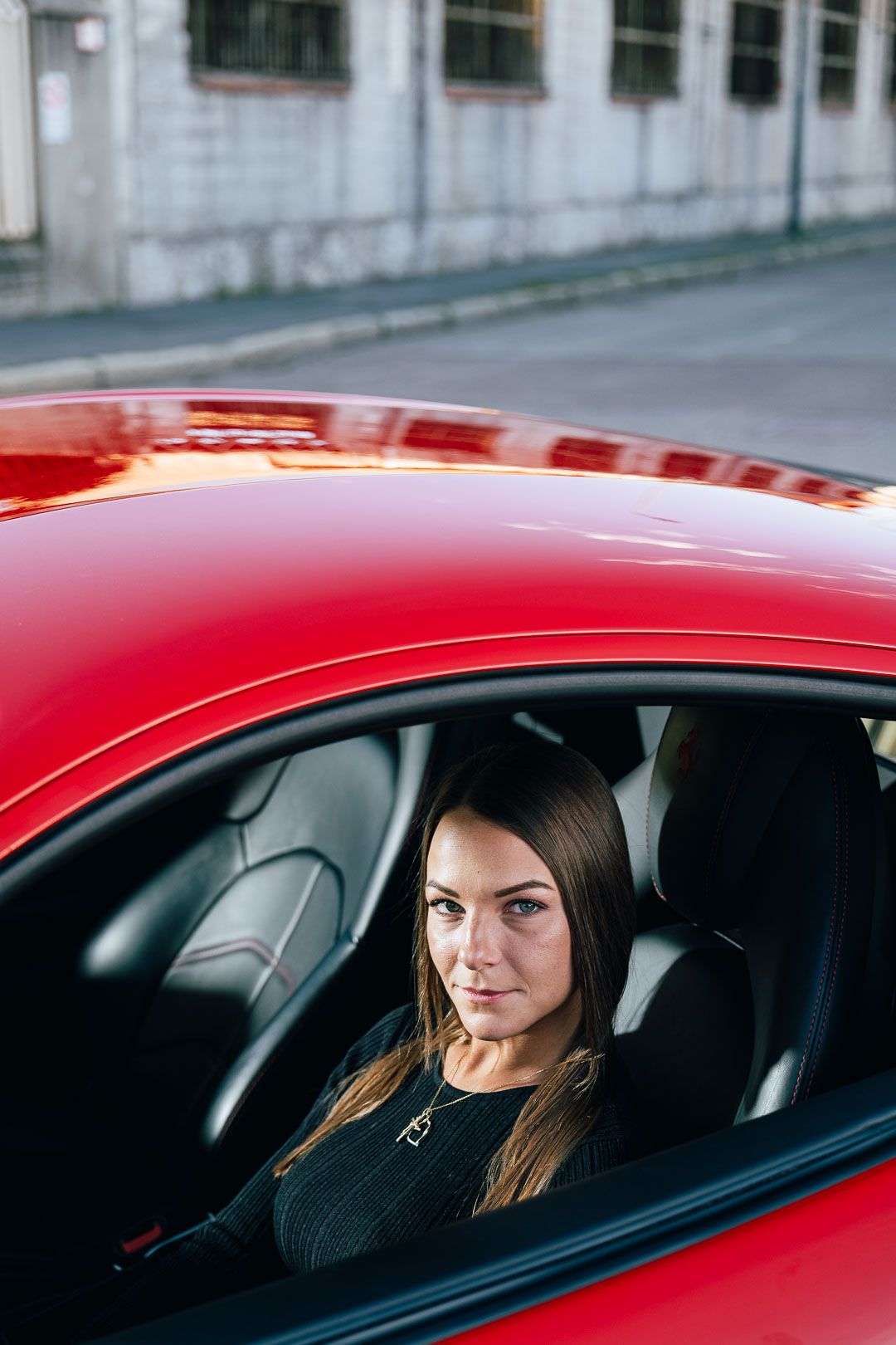 Woman sitting in red sports car looking through driver's side window.