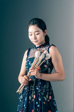 Young musician in floral dress holds collection of percussion mallets.