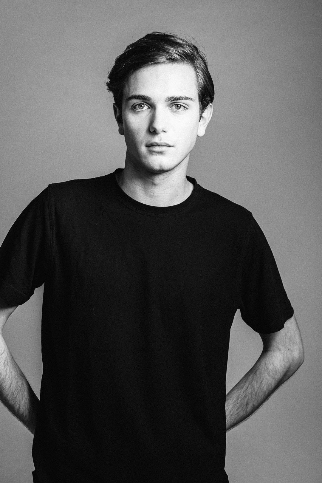 Black and white studio portrait of young man wearing simple black t-shirt.