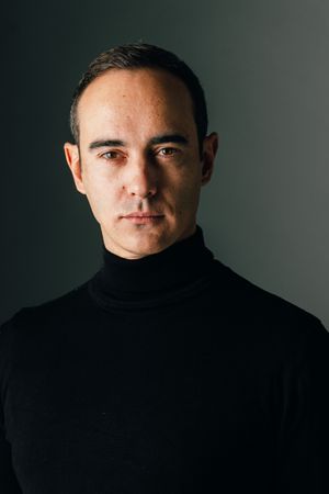 Studio portrait against dark background wearing black turtleneck.