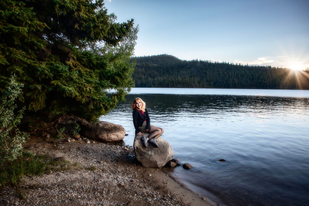 Peaceful lakeside scene with evergreen trees and sunset reflections on water.
