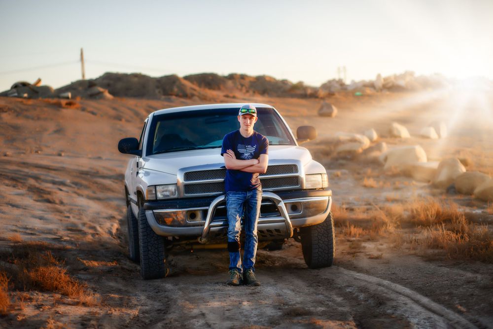 Someone leaning against a lifted pickup truck at sunset in a desert landscape.