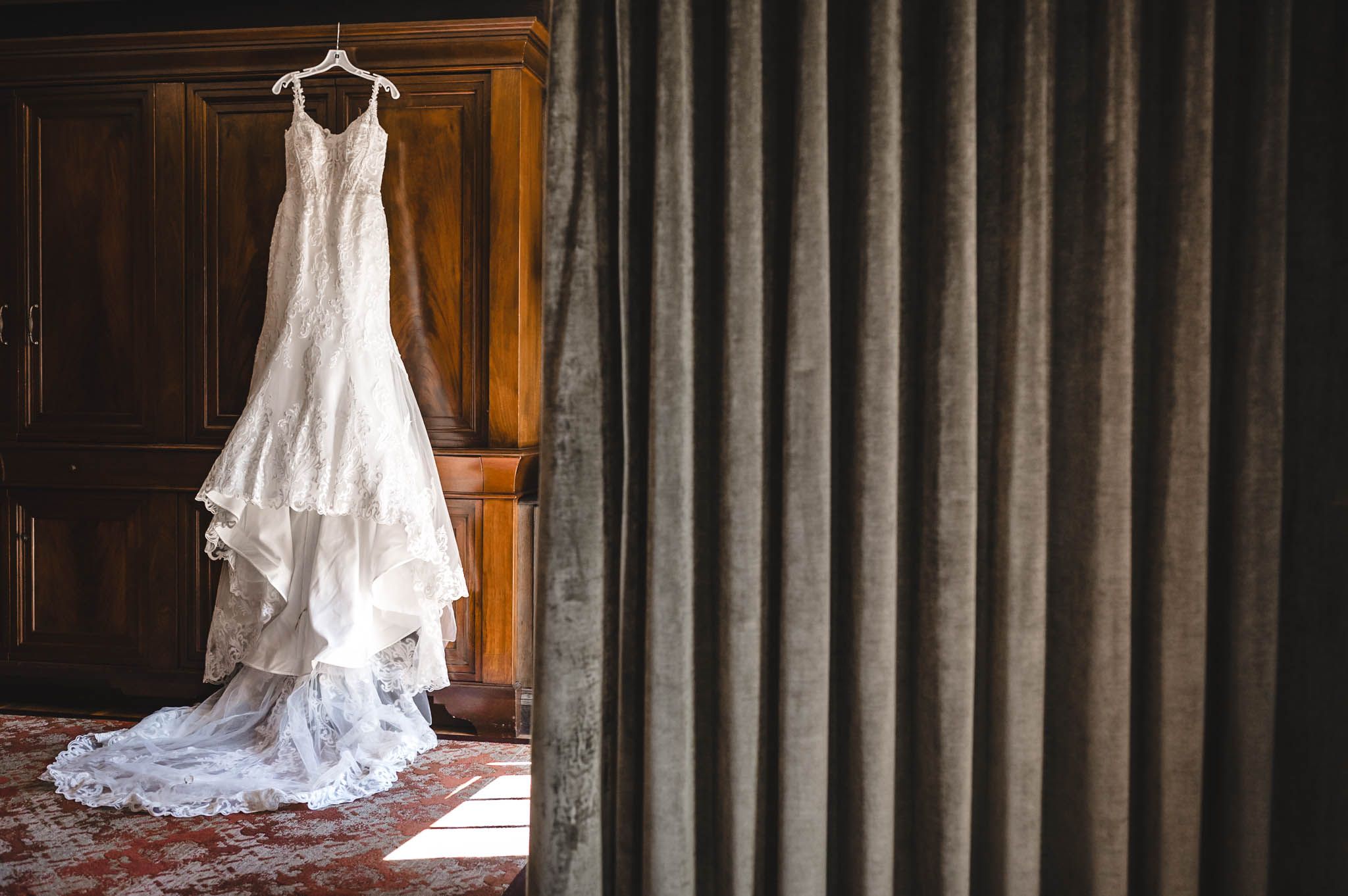 Elegant white wedding dress displayed against dark wood paneling with dramatic lighting.