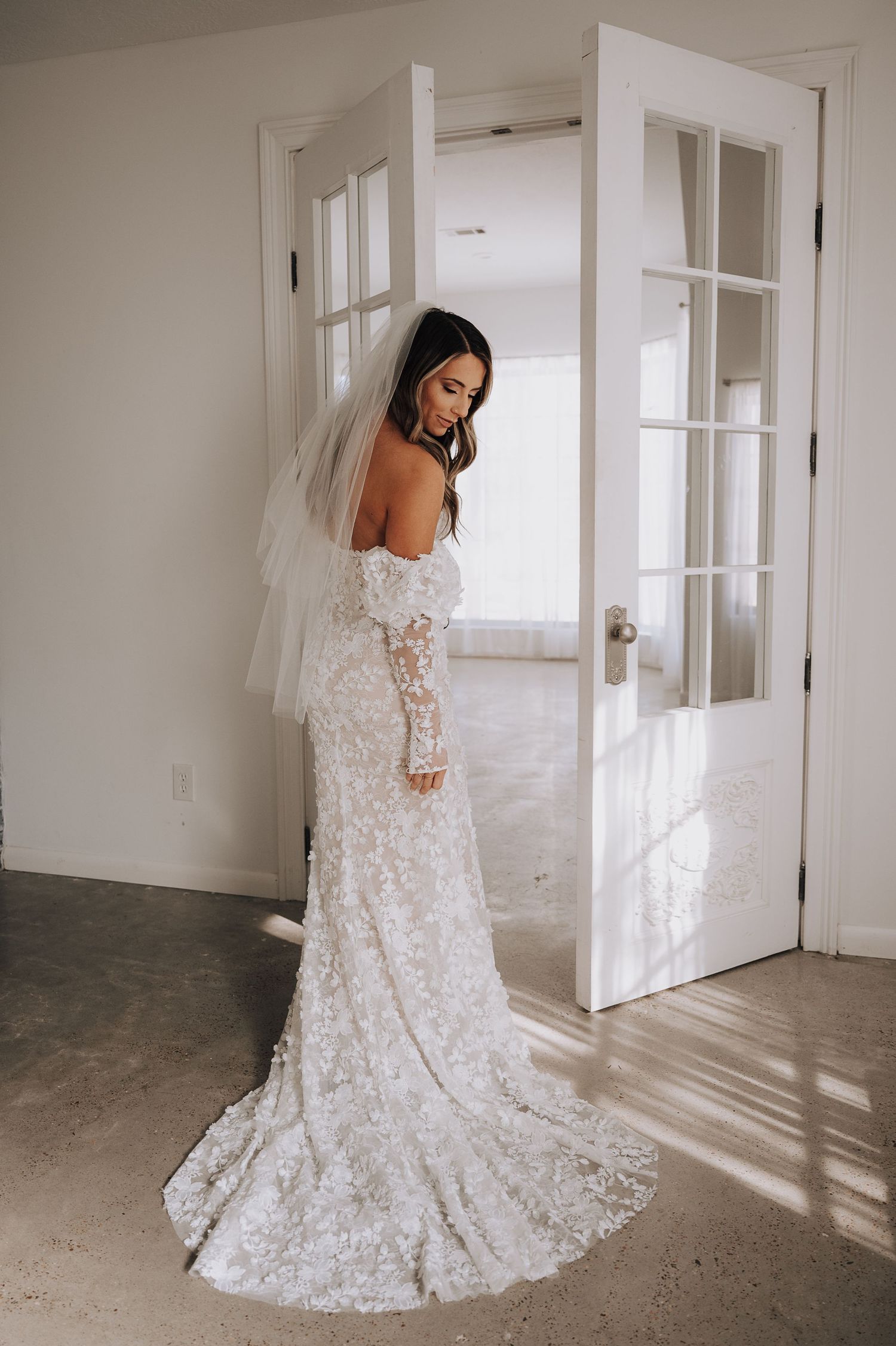 A lace wedding gown with long sleeves and train photographed in natural window light.
