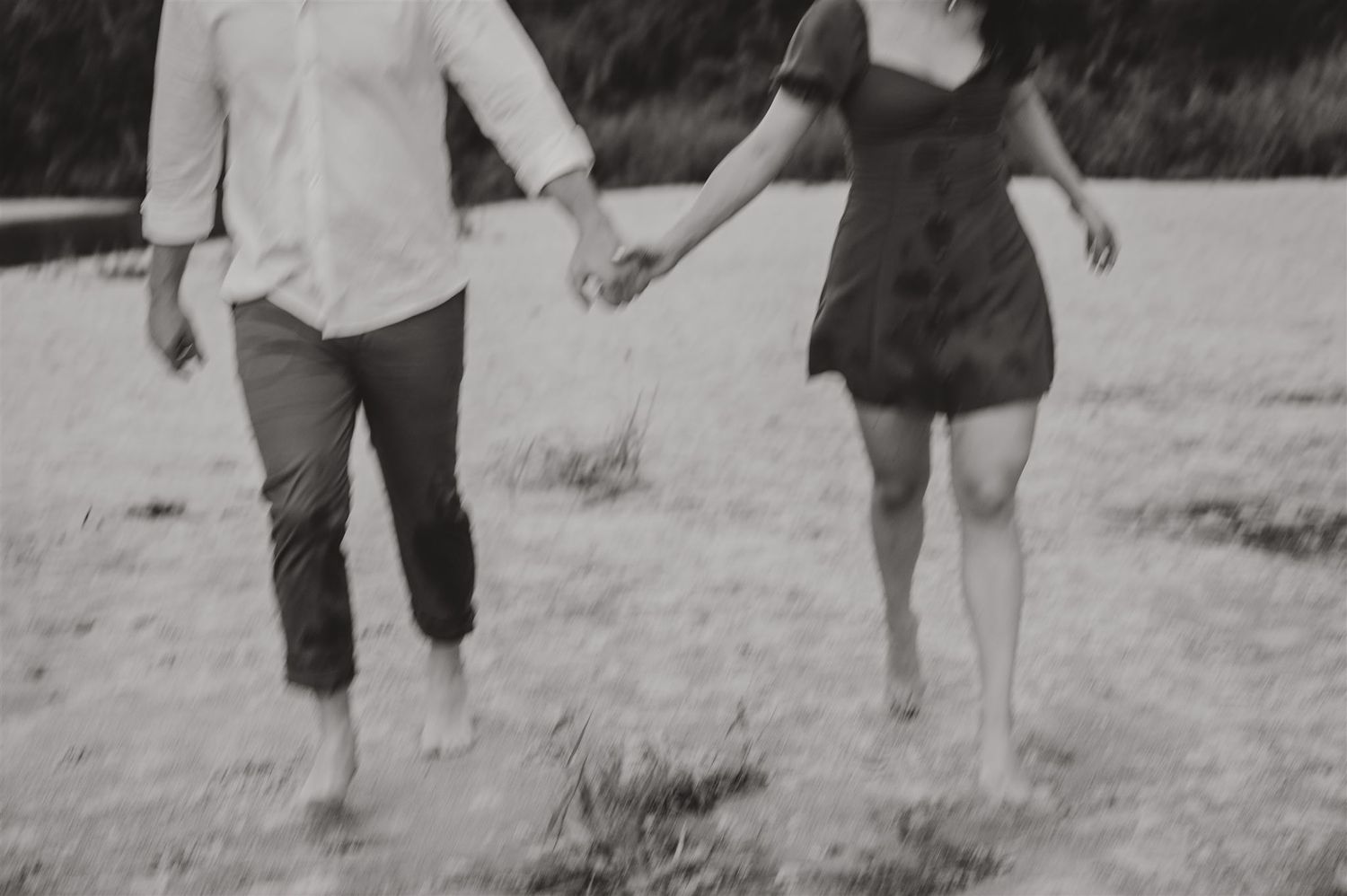 Black and white photo of a couple holding hands while walking barefoot together.