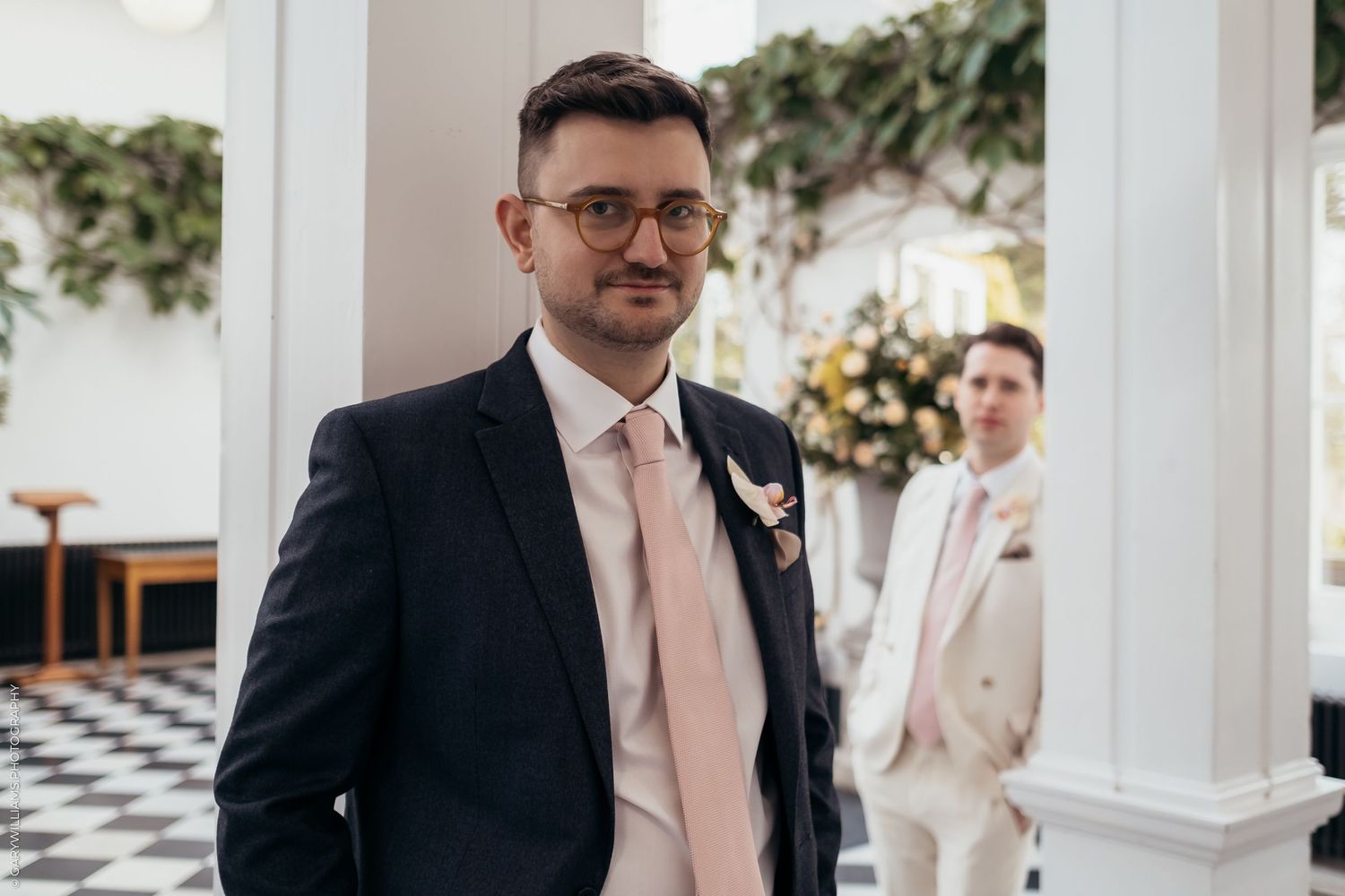 Newlywed grooms in suits in between white columns at their gay wedding in Twickenham London