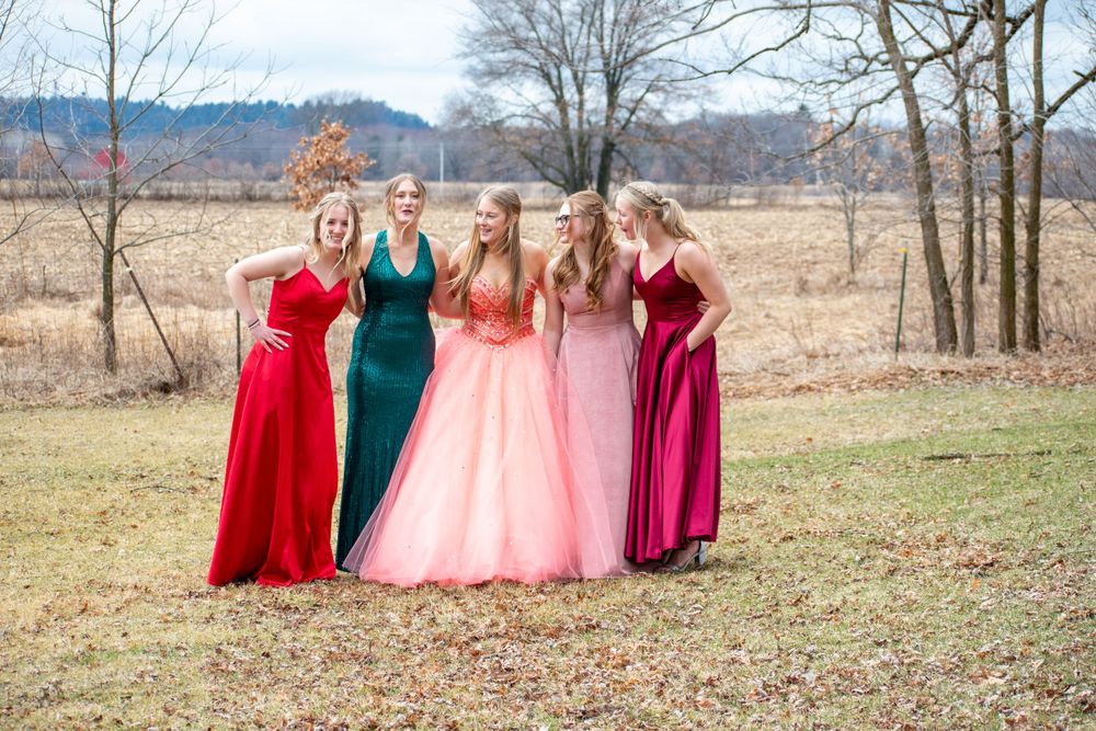 Group in formal dresses stands together in an open field during autumn.