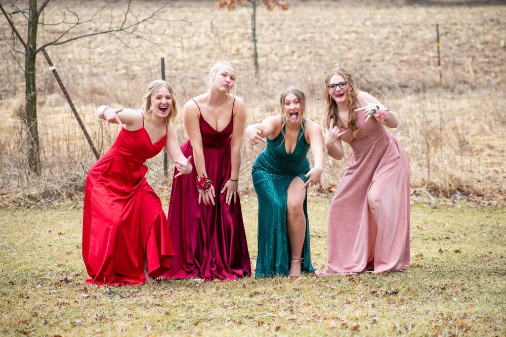Friends in colorful formal dresses pose together in a field during a photo shoot.
