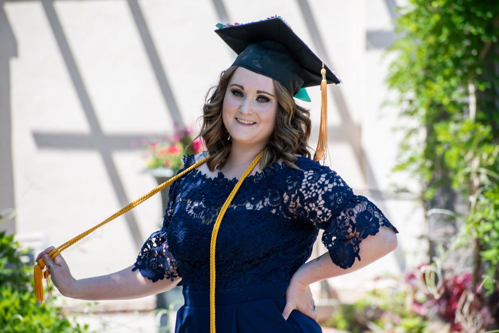 Graduate in navy dress and cap smiles brightly in outdoor graduation photoshoot.