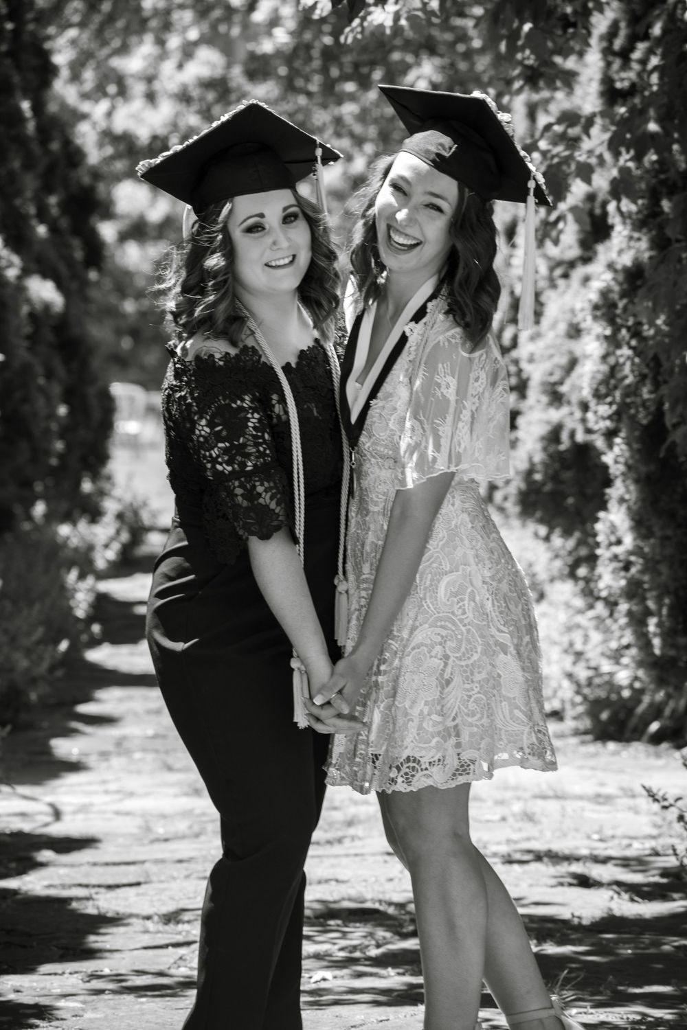Black and white photo of graduates posing together under trees in graduation attire.