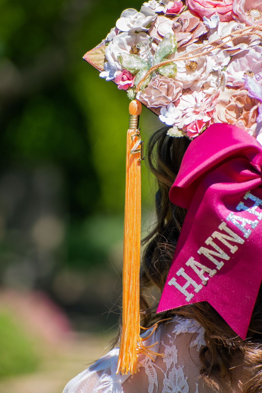 Decorated graduation cap with pink bow and gold tassel shown in detail.