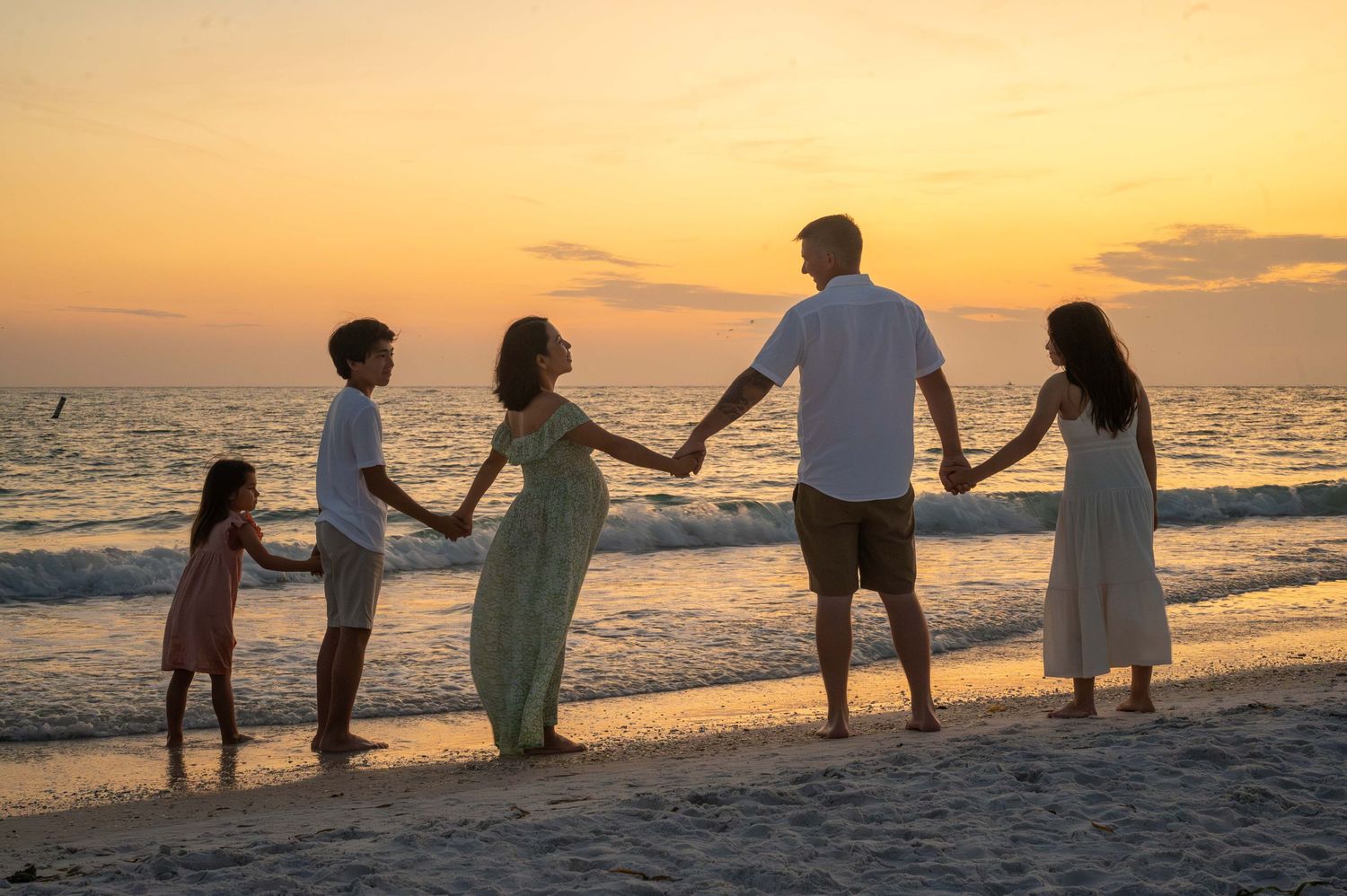 Silhouettes of a family holding hands on beach at sunset.