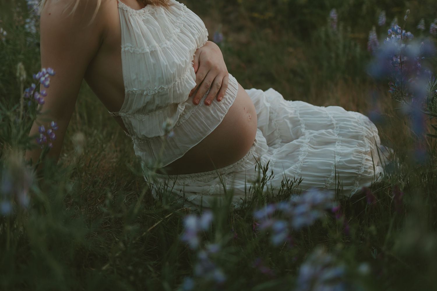 Ethereal maternity photo showing pregnant woman in white dress holding dried flowers.
