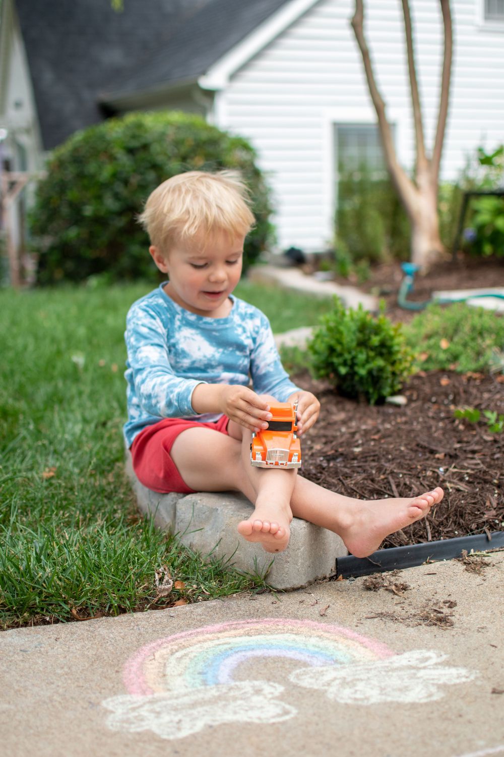 Playing with a toy car by a rainbow chalk drawing in a garden setting.