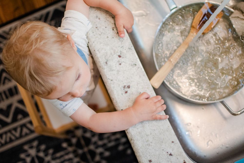 Helping in the kitchen while standing on a stool near the sink.