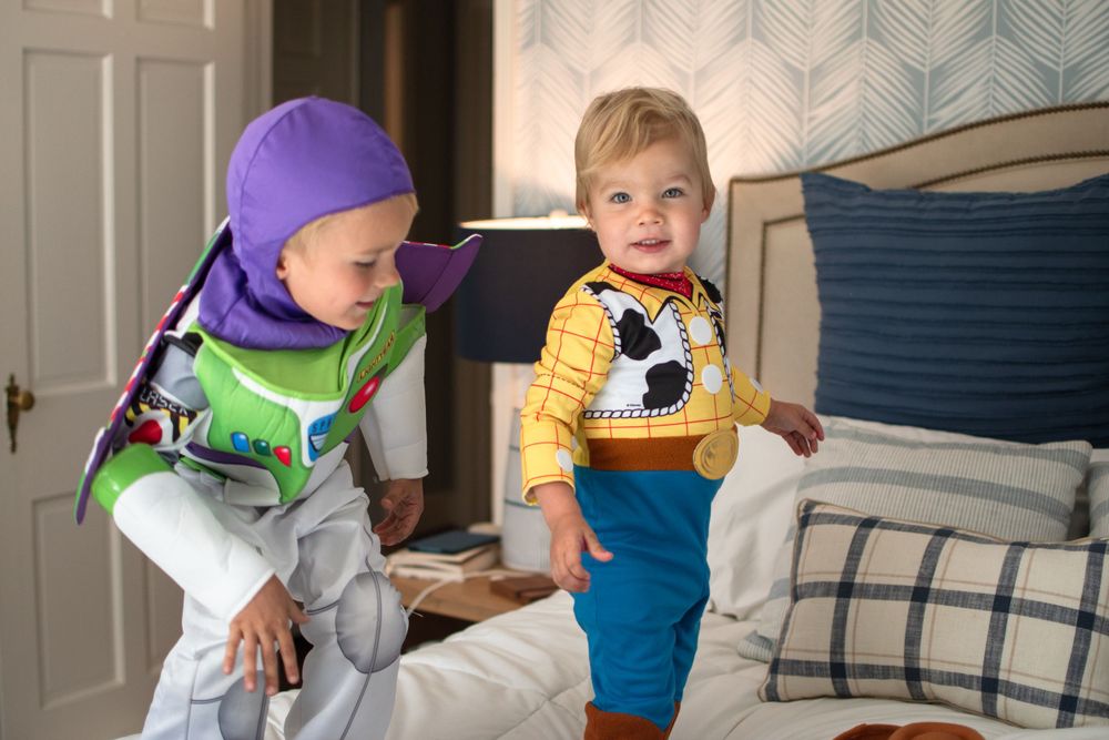 Two toddlers wearing Toy Story themed costumes play together on a couch with blue striped pillows.