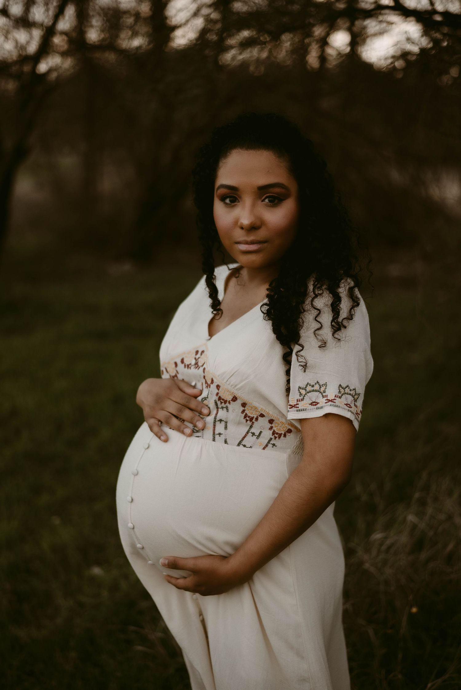 Twilight maternity photography featuring a flowing white dress with embroidered accents.