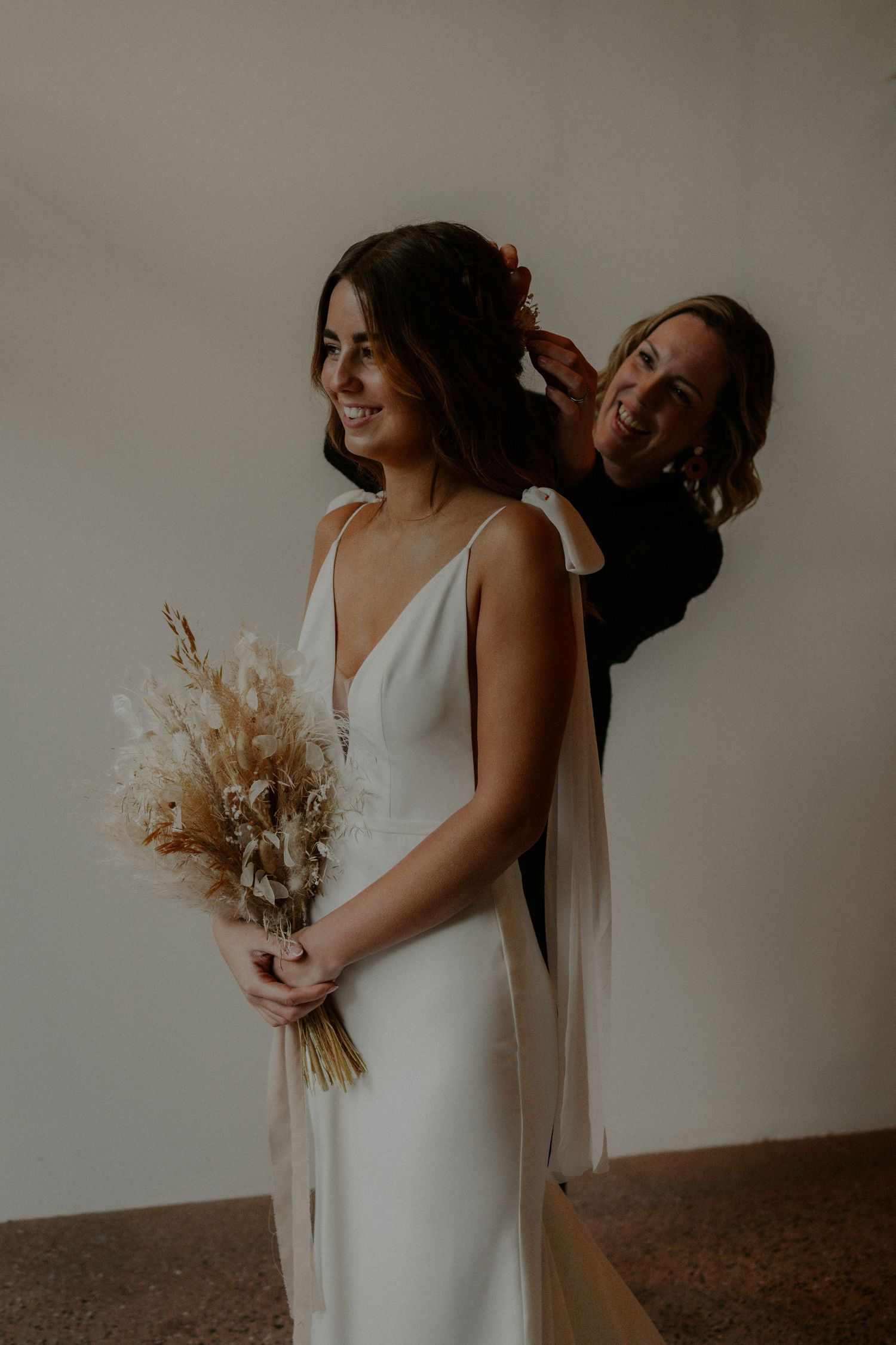 Two people sharing a joyful moment in white dresses with dried floral bouquet details.