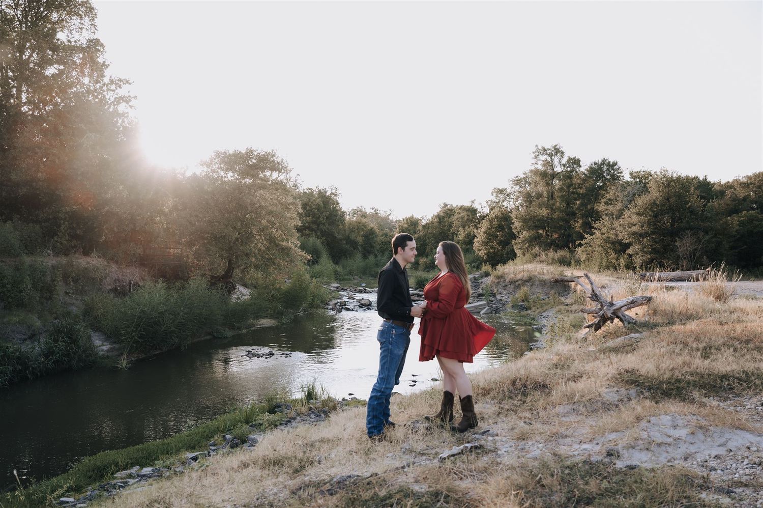 Sunset engagement session by a serene river with couple in casual attire.