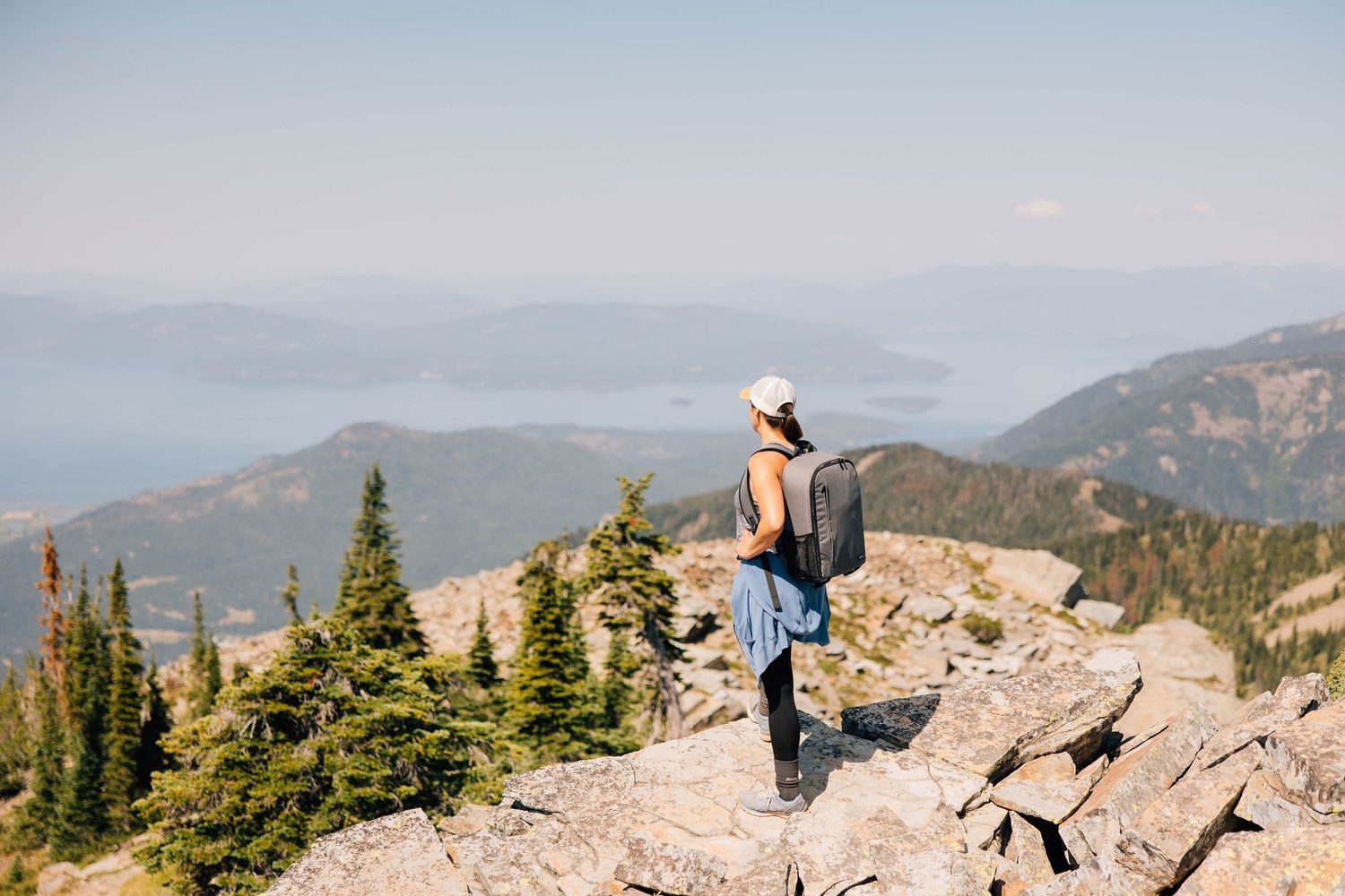 Hiker standing on mountain summit overlooking distant peaks and valleys.