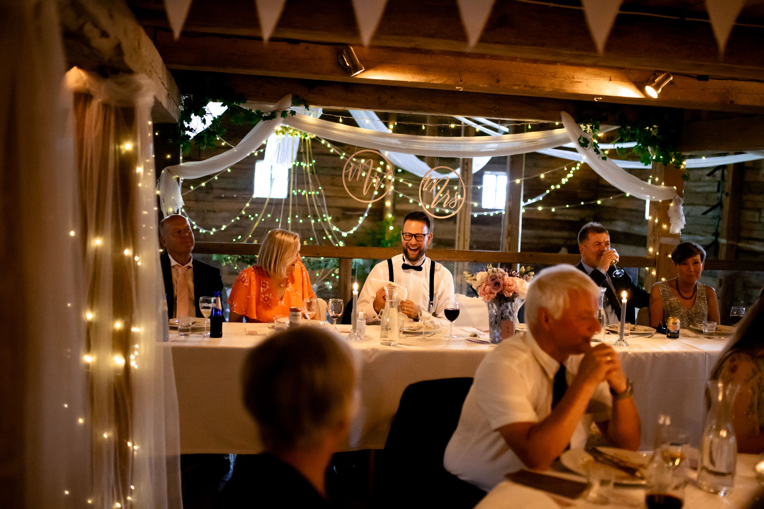Wedding reception venue decorated with string lights and white bunting in a rustic indoor setting.