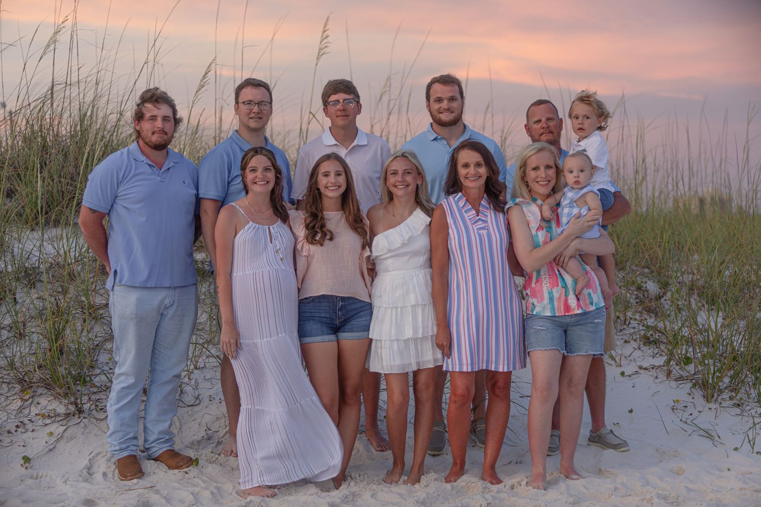 Group poses for casual beach photo at sunset wearing coordinated blue and white outfits.