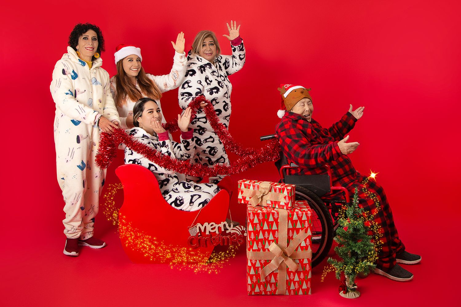 A fun family group poses in festive pajamas with Christmas decorations against a bold red background.