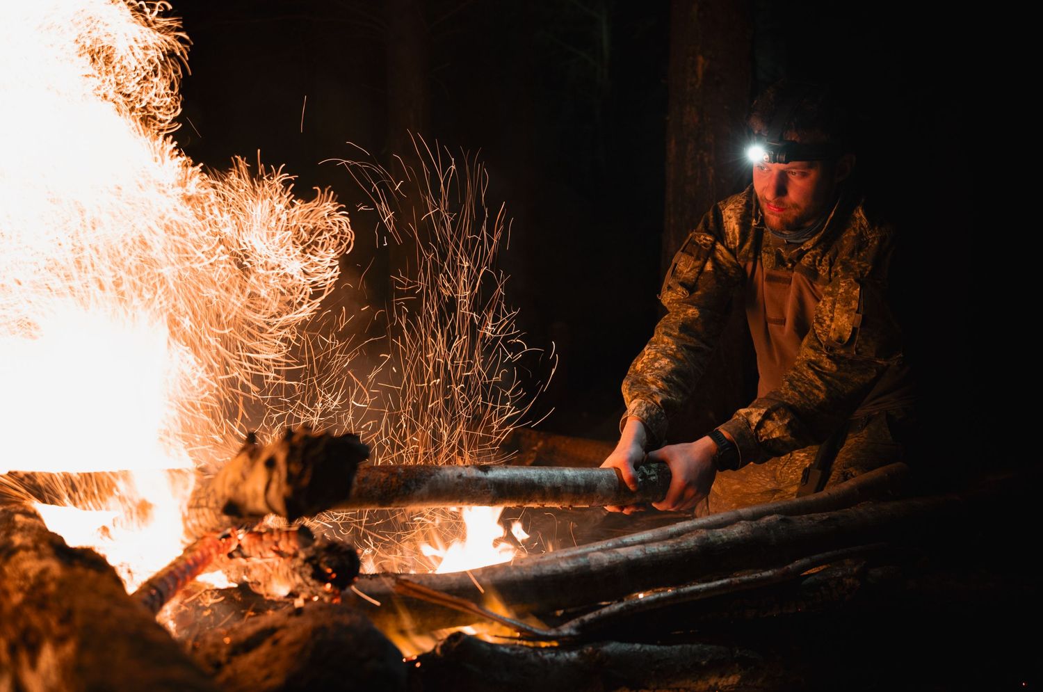 Person tending campfire at night with orange flames illuminating the darkness.