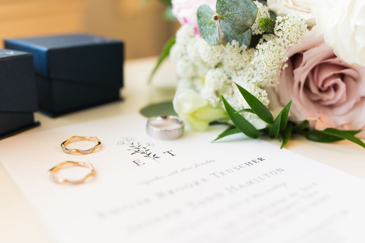 Wedding details featuring delicate floral arrangements, rings, and invitation paper on a white surface.
